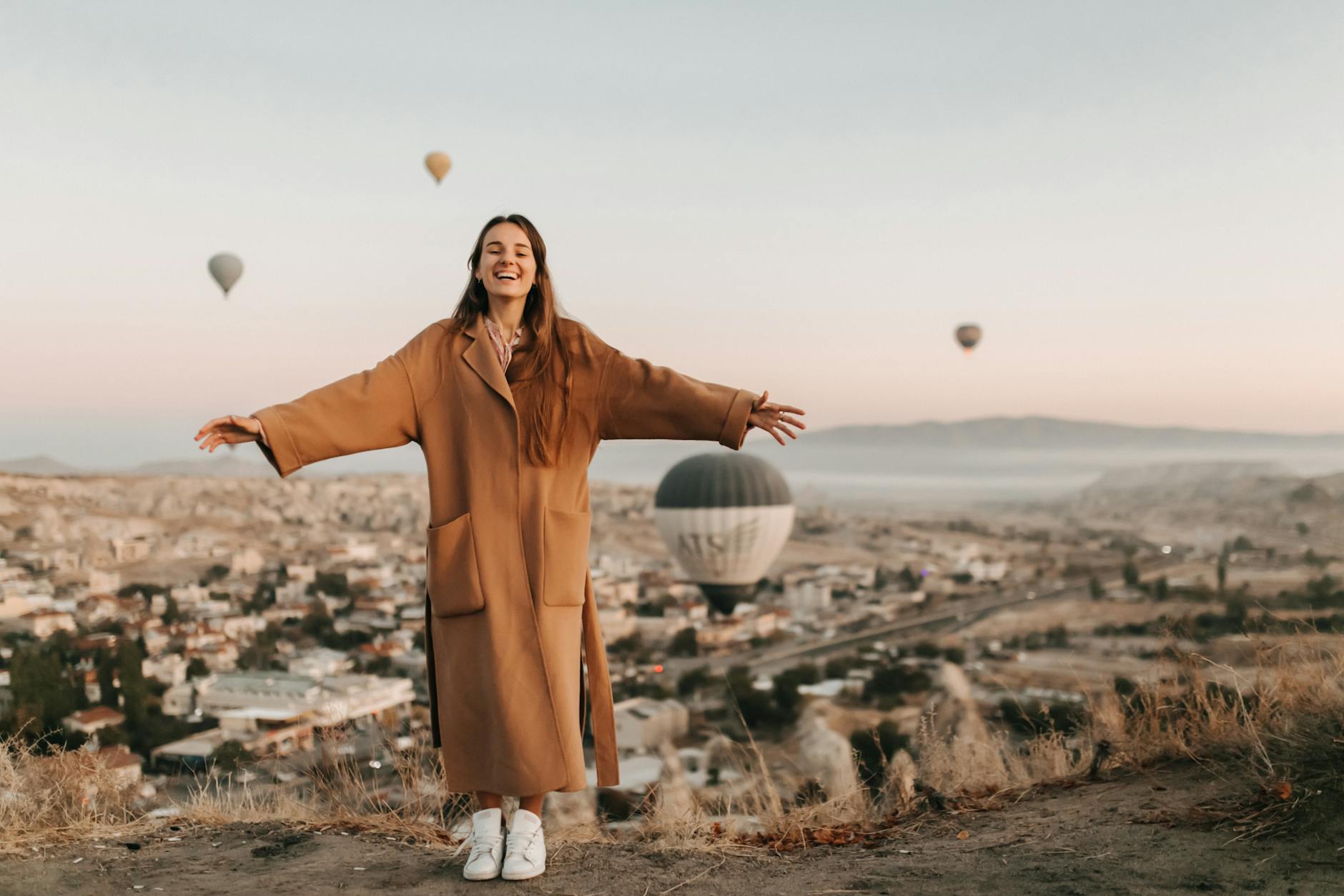 woman in brown coat standing on the ground open arms